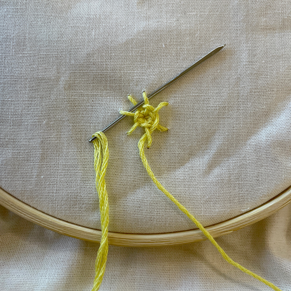 Roseblomst broderi med gult garn på råhvidt stof